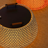 Nans Bag/38 Wood LED outdoor floor lamp with a round, drum-shaped brown woven shade, flat dark top, and two teak wood handles, glowing warmly outdoors.