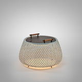 Nans Bag/38/R rechargeable outdoor floor lamp, a round woven basket shade in beige with light blue tint, dark lid and two wood handles, glowing LED light, on a plain light grey background.