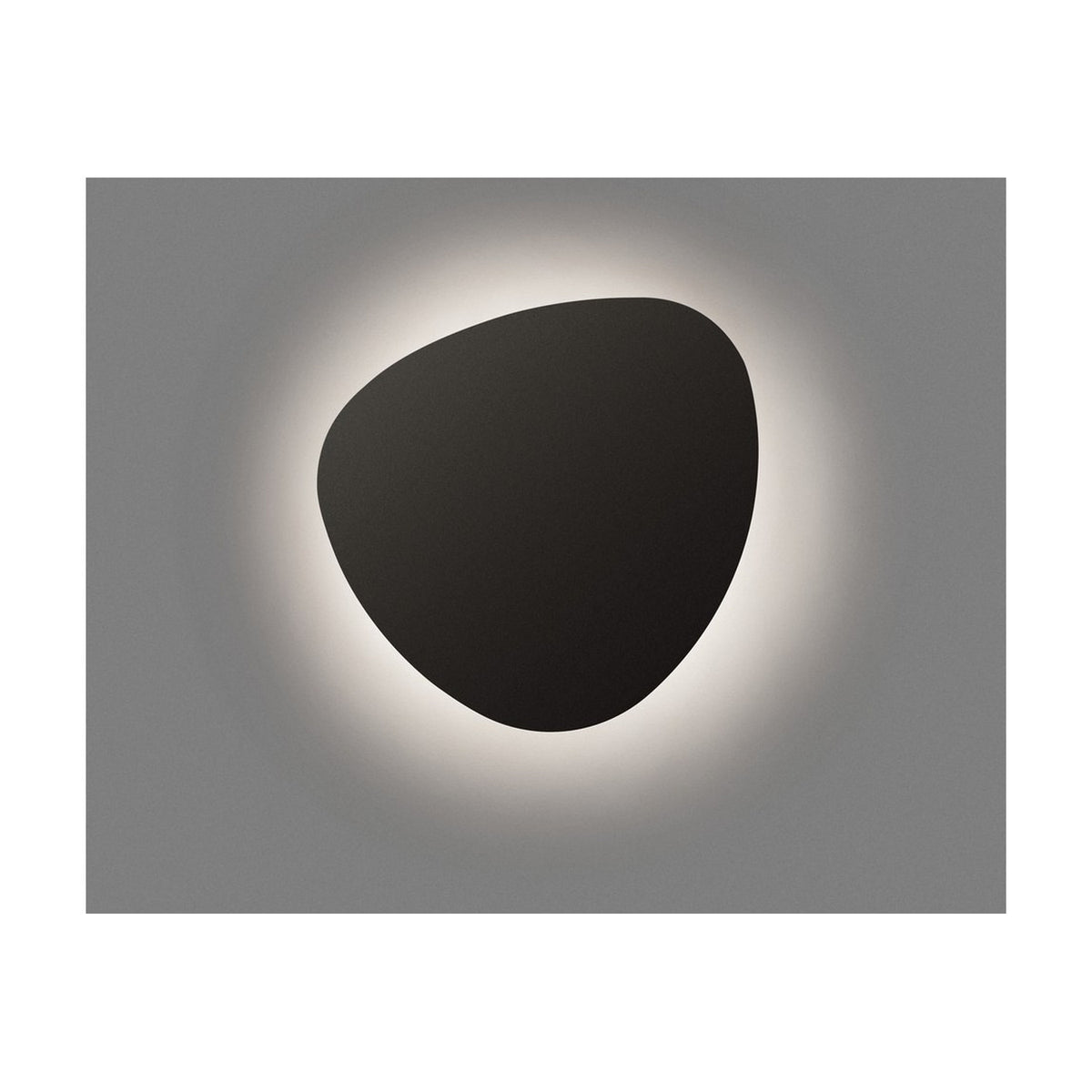 Tria 05 Wood outdoor wall light with a smooth, pebble-shaped graphite brown metal face and integrated LED casting a soft warm-white halo on the grey wall behind it.