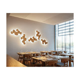 Tria 6 Light Wood LED Wall Light in natural oak, clustered pebble-shaped panels with warm backlit glow, shown installed above restaurant dining tables.