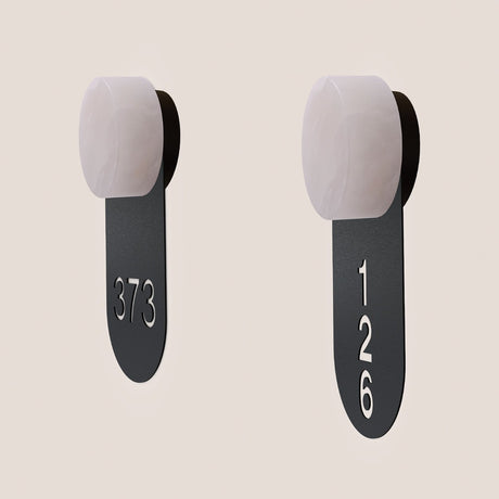 Two Rock wall lights with alabaster round heads and matt black iron signage tags cut with room numbers 373 and 126, shown on a plain light background.