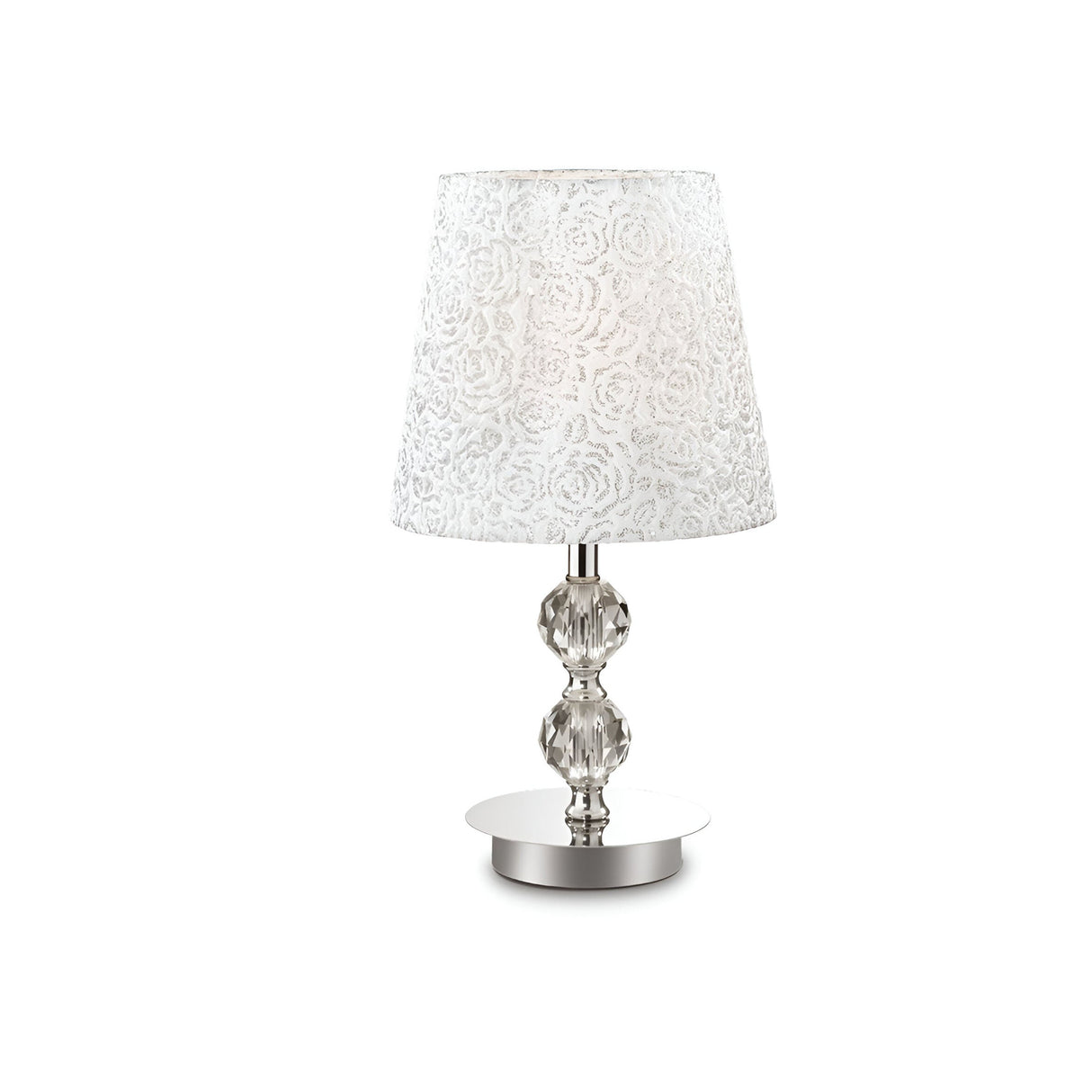 This elegant room decor piece, the Lumina Medium Crystal Table Lamp - Chrome, boasts a white fabric lampshade with a floral pattern set atop an ornate clear glass base. Ideal for modern classic style enthusiasts, it sits gracefully on a round metal platform against a plain white background.