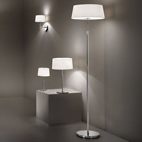 A contemporary lighting display showcasing minimalist design and elegance includes three lamps: a wall-mounted lamp, the Satin Small Table Lamp - White on a pedestal, and a tall floor lamp. Each features sleek metal stands and white cylindrical shades, set against a neutral gray backdrop.