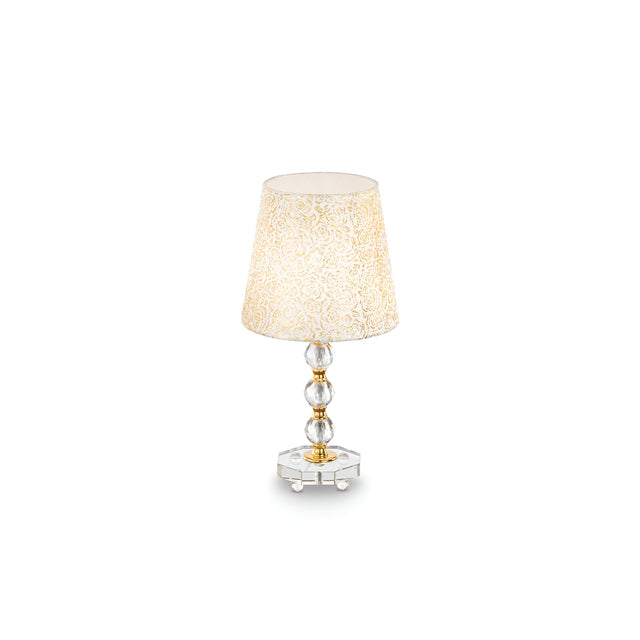 The Princess Medium Crystal Table Lamp - Gold, with an elegant glass base featuring round, stacked crystals and a beige intricately patterned shade, gleams against a plain white background.