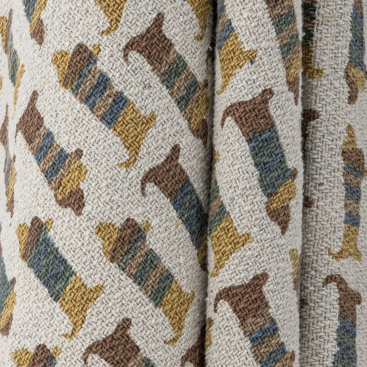 Charlie Cotton Throw in multicoloured fabric, woven with repeated striped sausage dog motifs, shown draped in close-up detail.