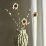 Poppy Artificial Stem in beige displayed in a ribbed sage ceramic vase, showing ruffled petals, dark centres, buds and slender twisting branches against a neutral backdrop.