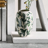 Birdliva Stoneware Vase 33cm in white with green bird and leaf motifs, rounded body and short rim, shown with foliage on a concrete plinth against a white backdrop.