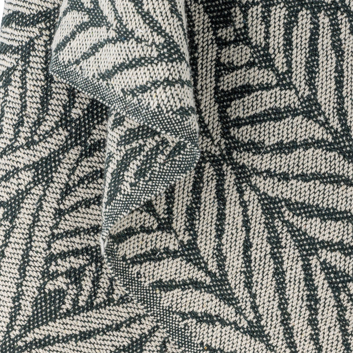Ugento Leaf Cotton Throw in green, close-up of the woven fabric showing tall overlapping fern-leaf patterns in dark green on an off-white cotton blend.