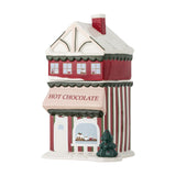 Gloria ceramic Christmas storage jar shaped like a hot chocolate shop, with red upper storey, snow-topped roof, chimney, and striped base, lid forming the house's top floor, on a white background.