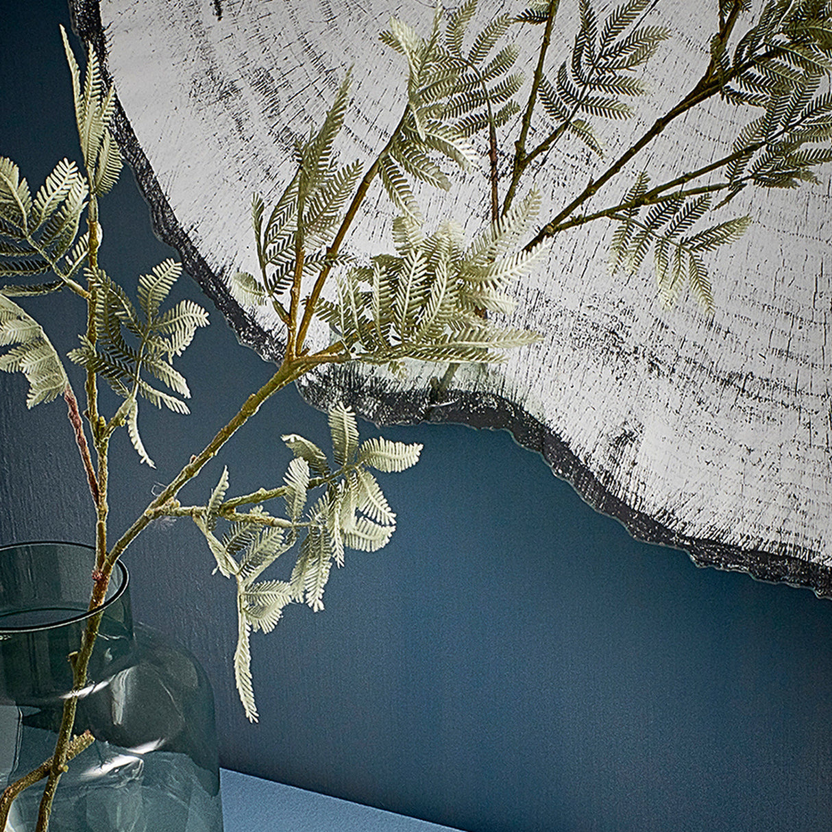 Close-up of the dark ragged edge with fern fronds crossing in front of it against a deep blue wall.