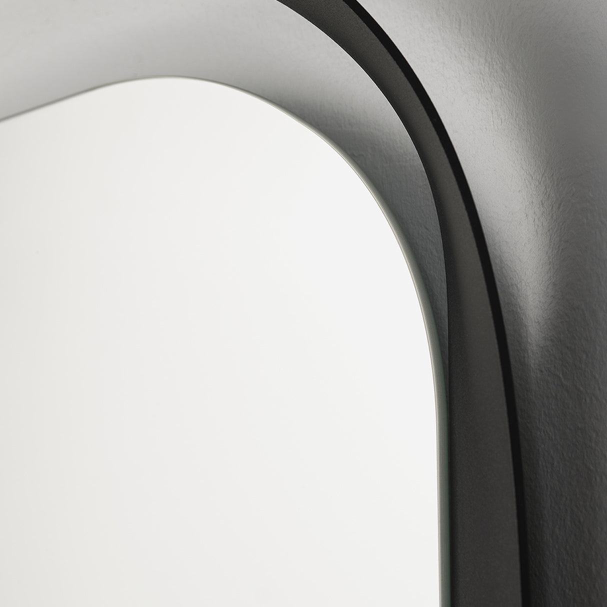 Close-up of the curved frame against the wall, showing the shadow the profile throws behind the oval glass.