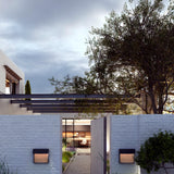 Sisal A/01 LED outdoor wall lights with woven brown fibre panels illuminated on a white brick garden wall, flanking an entrance gate at dusk.
