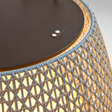 Close-up of the Nans Bag/38 outdoor floor lamp, showing its flat dark round top with control buttons and woven beige shade illuminated by integrated LED light.