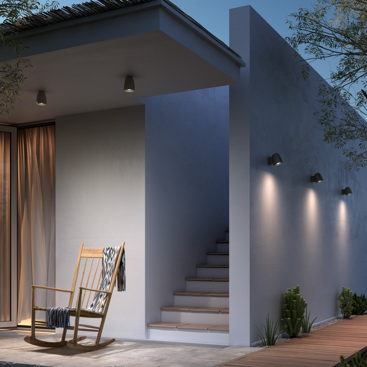 Three Nut A/01 stainless steel outdoor wall lights with bell-shaped black heads mounted on a grey exterior wall beside steps, each casting warm white downward light.