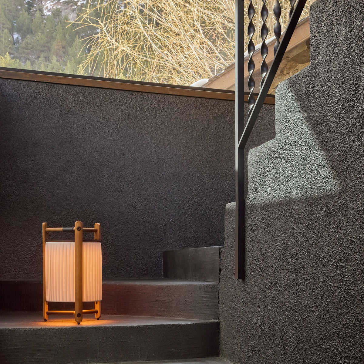 Kando P/76/R rechargeable LED floor lamp with pleated white ribbon shade in an open wood frame, glowing on an outdoor stone step at dusk.
