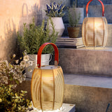 Tanit M/29/R rechargeable table lamps with woven beige fabric shades and red carry handles, lit on outdoor steps beside potted plants.