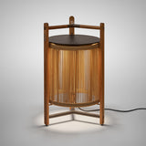 Kando P/76 outdoor floor lamp, lantern-style with sand nautical cord cylinder, teak wood tripod frame, dark round top and handle, illuminated, on a plain light grey background.