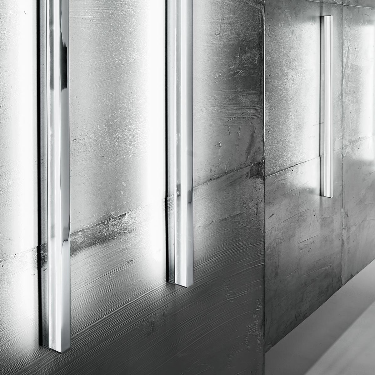 Zero Line Metal Linear LED Wall Light in chrome, slim vertical bars mounted on a textured concrete wall casting soft linear light bands.