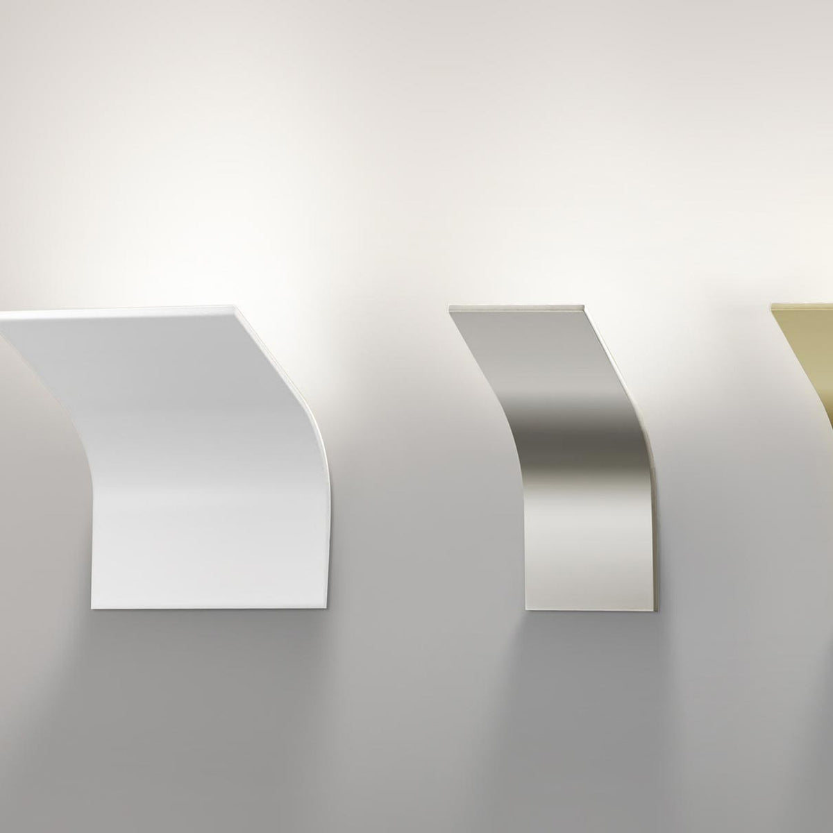 App Aluminium LED Wall Light shown in white, brushed silver, and brass finishes, each a curved aluminium plate wall light, displayed side by side on a plain light grey wall.