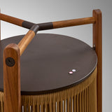 Close-up of the Kando M/40/R rechargeable outdoor table lamp showing teak wood uprights, dark metal top with control button, and sand-coloured cord shade.