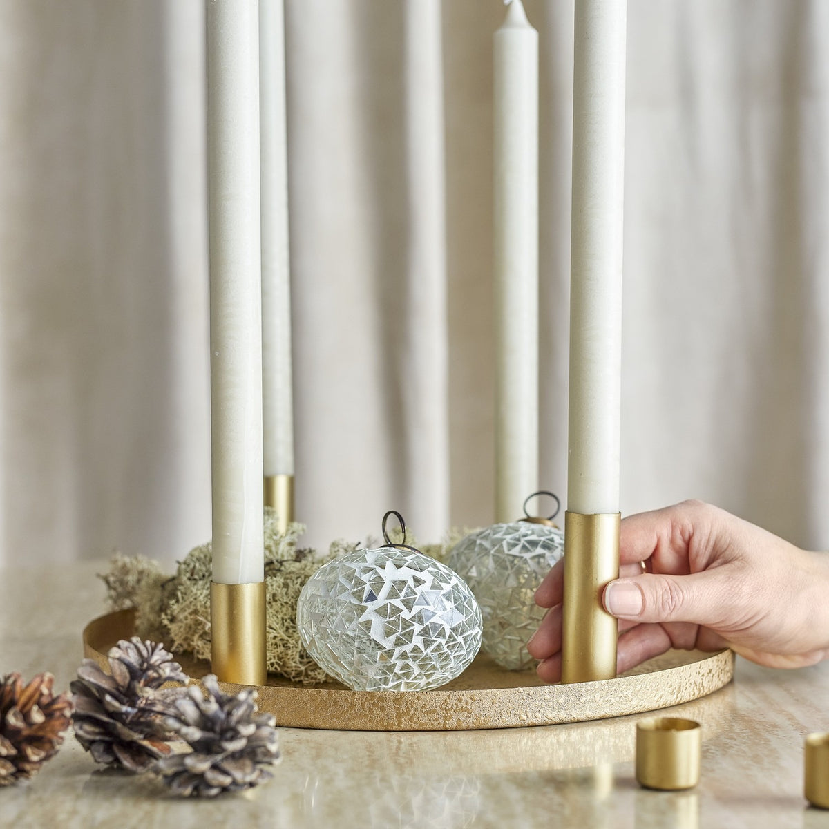 Maxime Iron Christmas Candle Holders Set of 7 in gold, round textured tray with slim tube holders and white taper candles, styled with moss, pinecones and mosaic baubles.