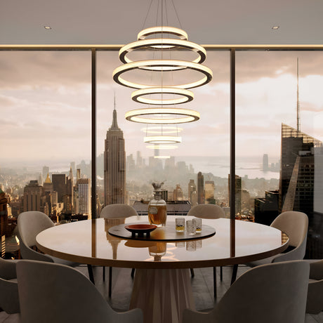 A luxurious dining area features a round table and elegant chairs, overlooking a city skyline. Above the table hangs a modern Celine LED Five Suspension Light in Gold, accompanied by a decanter and two glasses. Tall windows showcase the skyscrapers at sunset, enhancing the opulent atmosphere.