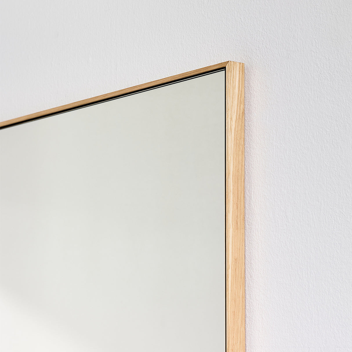 Close-up of the oak frame edge, the pale timber running along the glass with the mitre visible at the corner.