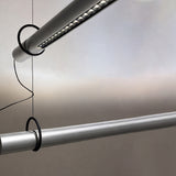 Close-up of the Solid SH 100 tube LED pendant light showing aluminium tubes with integrated LED strip, suspended level on fine wires against a neutral background.