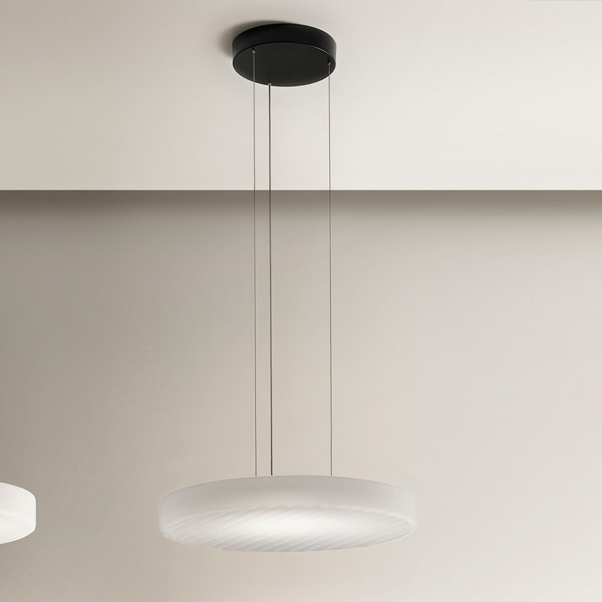 Côte LED pendant light with a shallow frosted white glass disc shade, ribbed underside, and black ceiling canopy on three thin cables, shown against a neutral wall.