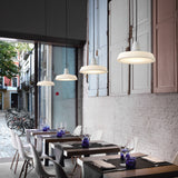 Marietta S/32 Dome LED Outdoor Pendant Light in white, shown in multiples over restaurant dining tables, with pleated dome shades, white necks, and black cables against a whitewashed wall.