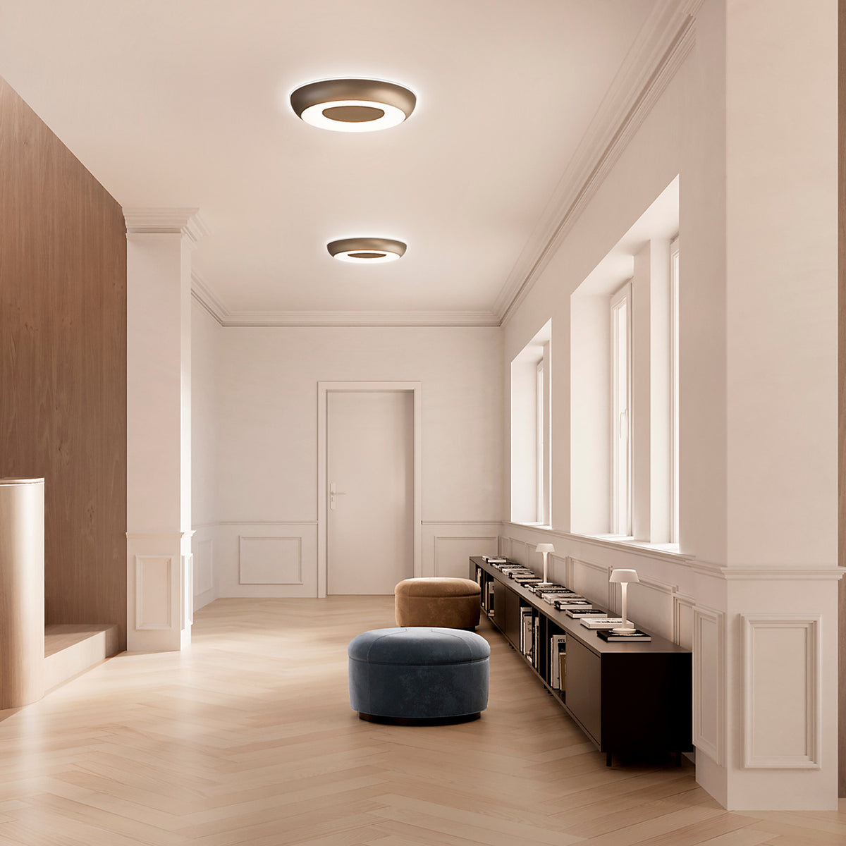 Two round Superbold LED ceiling lights in bronze finish, 44.3cm, illuminating a hallway with wood flooring, a dark sideboard, and velvet poufs.