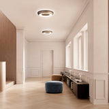 Two round Superbold LED ceiling lights in bronze finish, 44.3cm, illuminating a hallway with wood flooring, a dark sideboard, and velvet poufs.