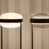Beaded T Glass LED table lamps with flattened spherical shades in opal white (lit) and smoke grey, each with a dark centre band and slim rod legs on a round base.