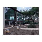 Cornet B/27 Cone LED bollard lights in Stone Grey with wavy tiered shades, glowing warm white along a garden path beside a glass-fronted house.