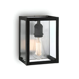 The Drape Wall Lights - Black is a contemporary lighting fixture with a sturdy black metal rectangular frame and a clear glass enclosure, housing an exposed vintage-style Edison bulb. Mounted on a white wall, it offers both style and timeless appeal.
