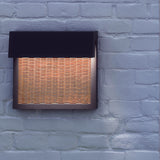Sisal A/01 LED outdoor wall light with a woven brown fibre front panel in a square frame beneath a dark hood, illuminated on a light grey brick wall.