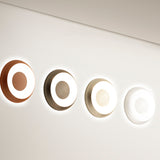 Four round Superbold LED wall and ceiling lights, 44.3cm, in copper, bronze, champagne and white finishes, each glowing with a soft white halo ring on a light wall.