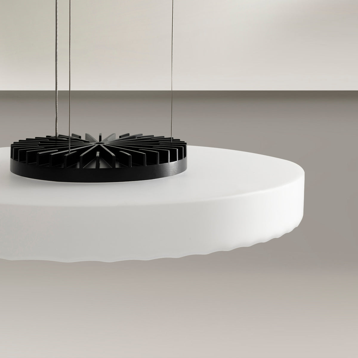 Close-up of the Côte frosted white glass LED pendant light's round disc shade and black finned heat sink, suspended by thin cables against a neutral background.
