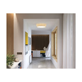 Plafonet 60 Ribbon LED ceiling light with a wide, shallow pleated cream drum shade, shown flush-mounted in a hallway with wood slat panelling and white walls.