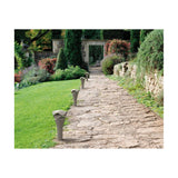 Cornet B/52 Cone LED Bollard Light in stone grey lining a stone garden path, with a slender flared cone base and wavy layered cap.