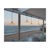 Marietta S/32 white dome-shaped outdoor pendant lights with pleated shades on black cables, hung in a row under a beachside canopy at dusk.
