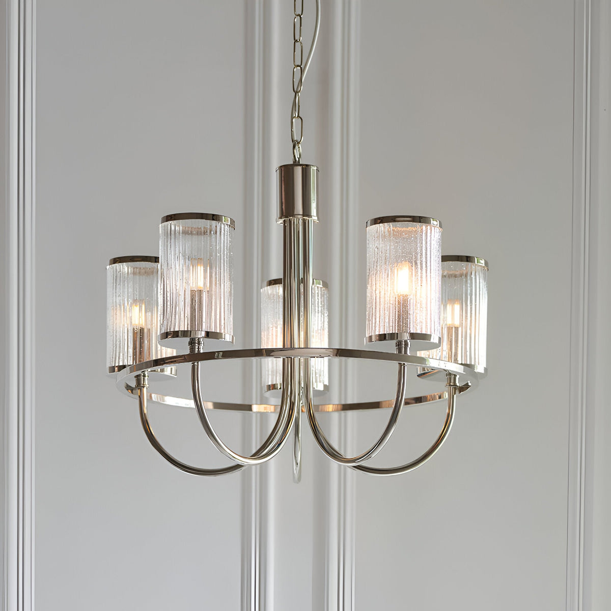 Endon Brenfield 5 light nickel pendant with curved arms and ribbed bubble glass cylindrical shades, suspended from a chain against a pale panelled wall.
