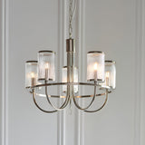 Endon Brenfield 5 light nickel pendant with curved arms and ribbed bubble glass cylindrical shades, suspended from a chain against a pale panelled wall.
