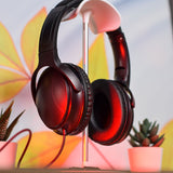 AV:Link QDJH-40 wired DJ headphones in black resting on a stand with red lighting, beside small potted succulents and a leaf-patterned backdrop.