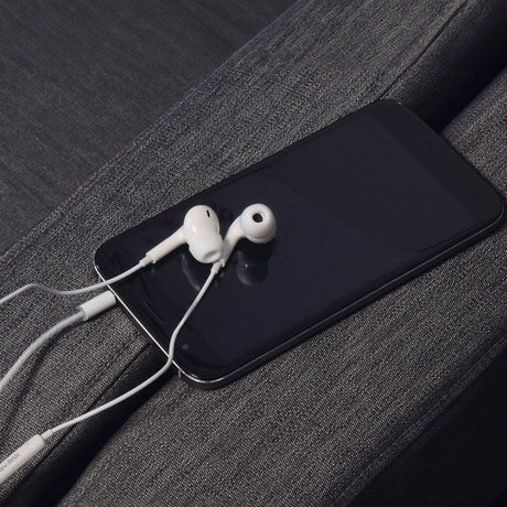 AV:Link Digital 3.5mm wired earphones with mic in white, resting on a dark smartphone screen placed on grey fabric upholstery.
