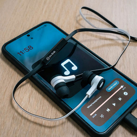 AV:Link rubberised stereo earphones in white with black tips and flat black cable, inline mic control resting on a smartphone playing music on a wooden desk.