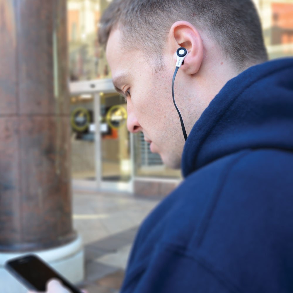 Man in navy hoodie wearing AV:Link rubberised stereo earphone with inline mic, black flat cable trailing down, using a phone outdoors.
