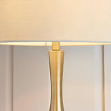 Close-up of the Endon Chartbury LED table lamp showing the slim brushed brass stem and beige fabric drum shade lit with warm white light.