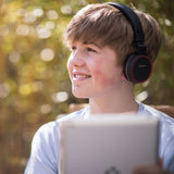 Young person wearing AVSL AV:Link PH10-BLK matt black headphones with red trim and cushioned earcups, smiling outdoors while using a tablet.