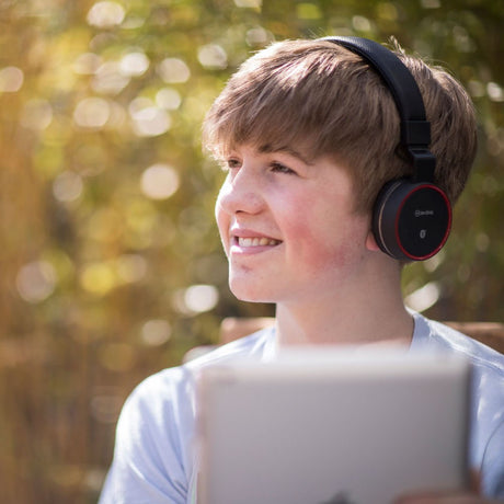 Boy wearing AV:Link PBH10-BLK Wireless Bluetooth Folding Headphones in matt black with red trim, shown outdoors with a blurred sunlit background.